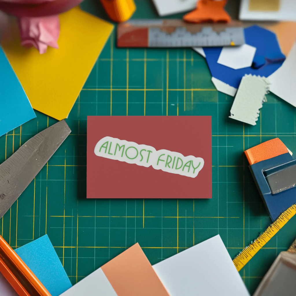 Card with 'Almost Friday' sticker on a cutting mat with crafting supplies. Durable vinyl die-cut.