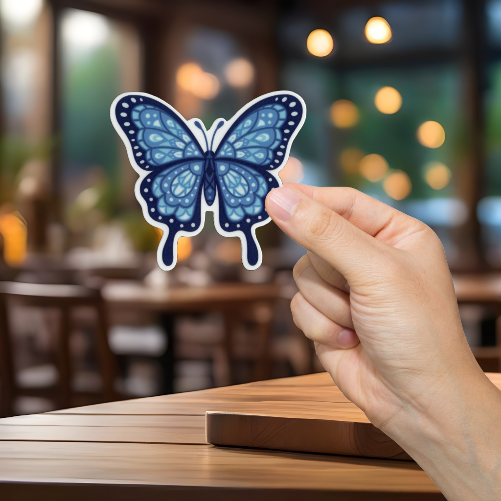 Hand holding a blue butterfly sticker with a blurred restaurant background