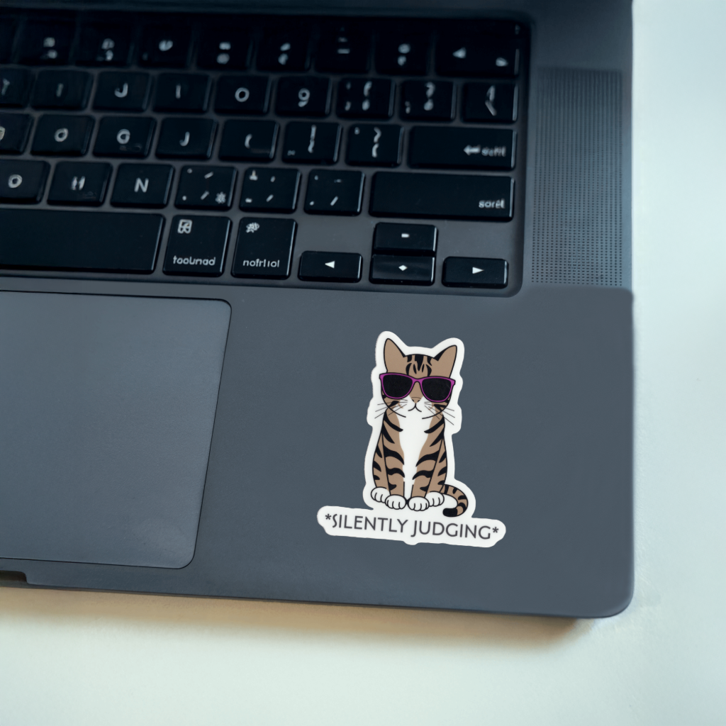 Laptop with a cat sticker labeled 'Silently Judging'. Durable vinyl, die-cut sticker.
