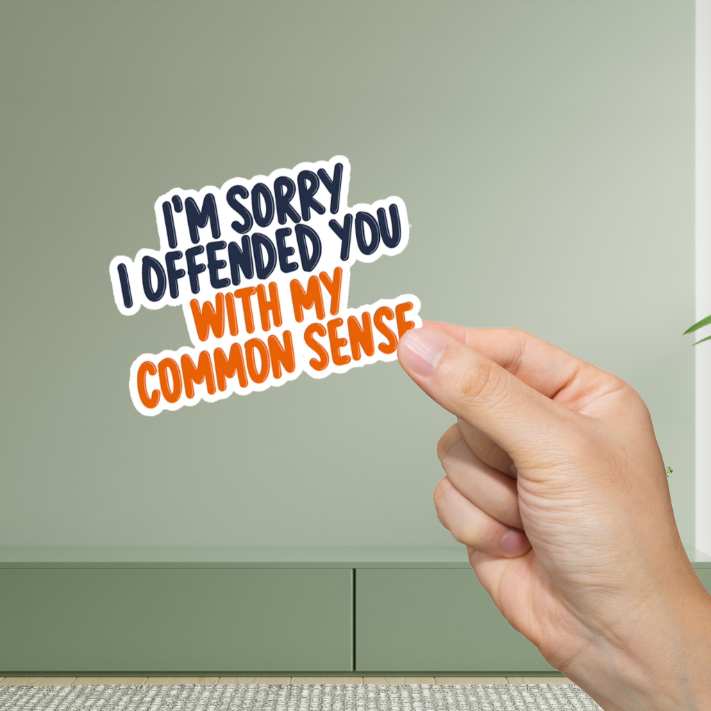 Hand holding a sticker with text 'I'm sorry I offended you with my common sense' against a green background