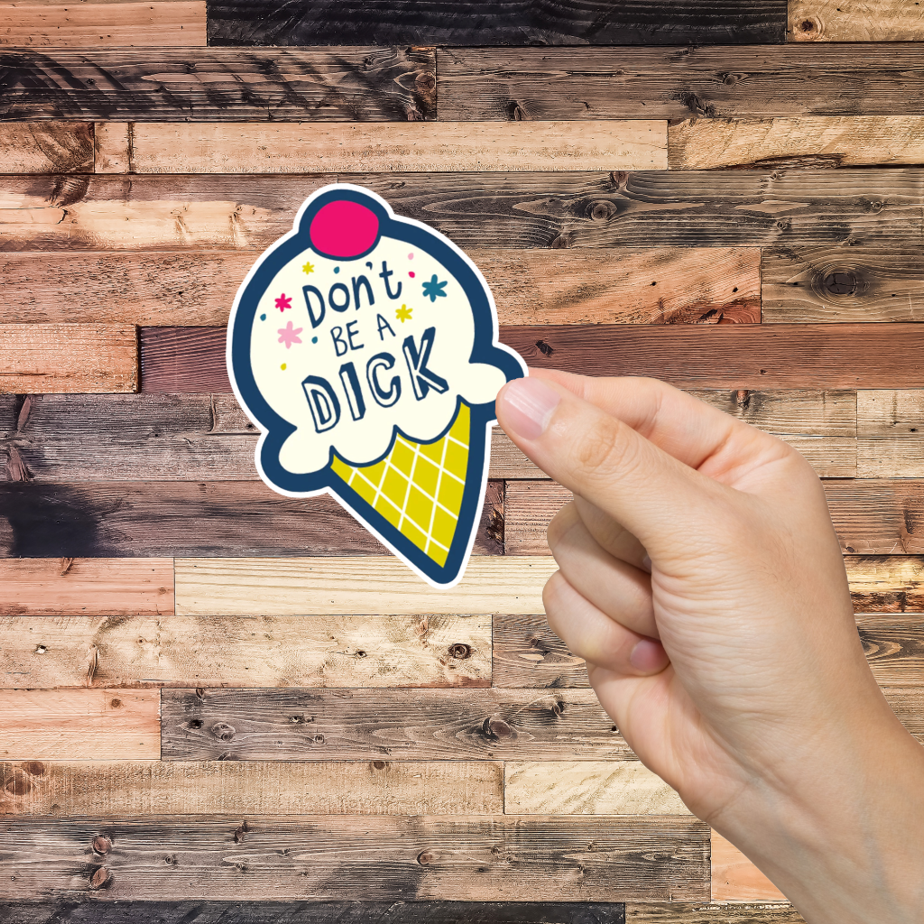 Hand holding a sticker with 'Don't be a dick' text against a wooden background