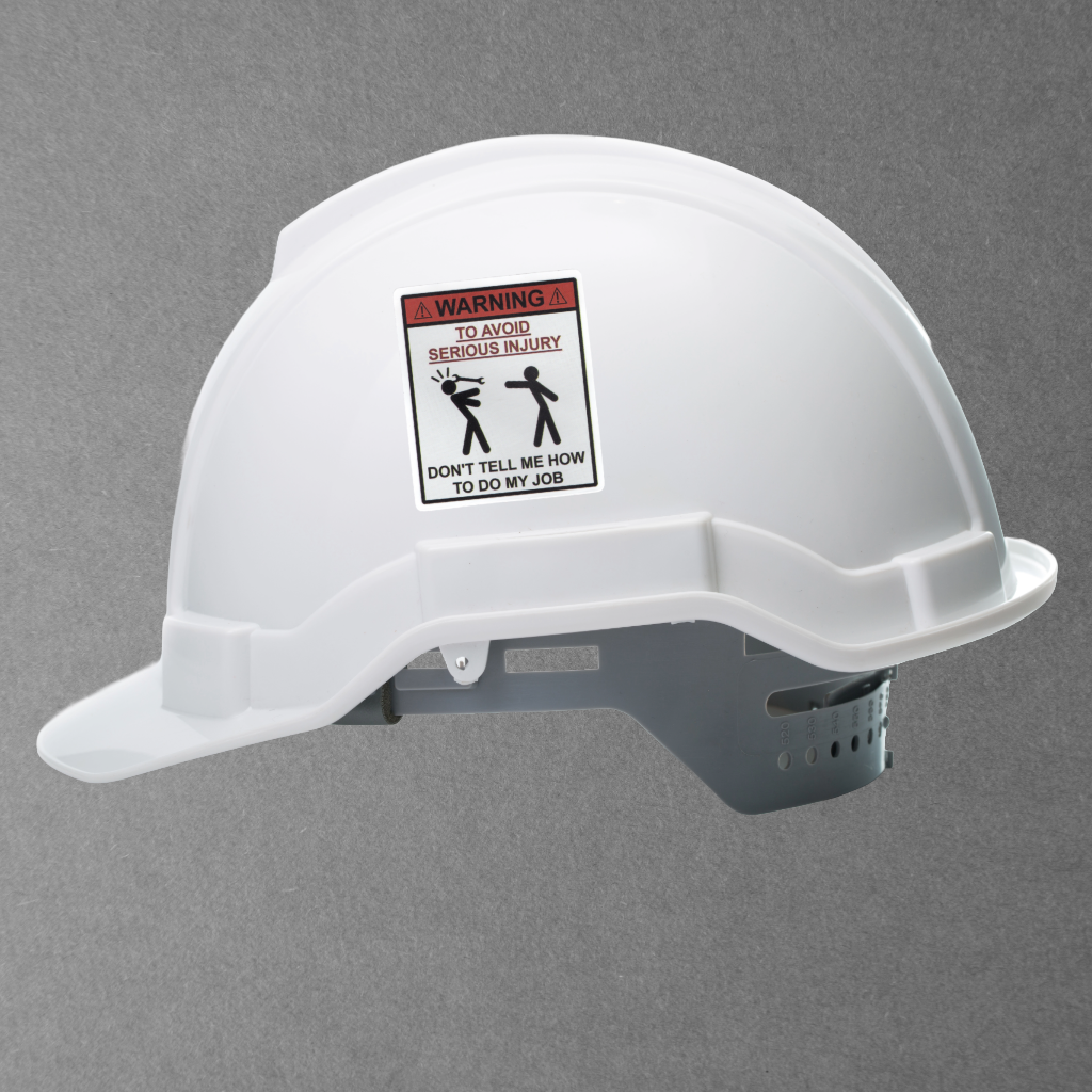 White hard hat with a humorous Avoid Injury safety sticker on a gray background