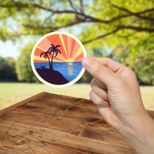 Hand holding a round sticker with a tropical design on a wooden surface with a blurred natural background
