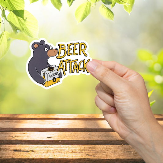 Hand holding a sticker with a bear and 'Beer Attack' text against a blurred green outdoor background