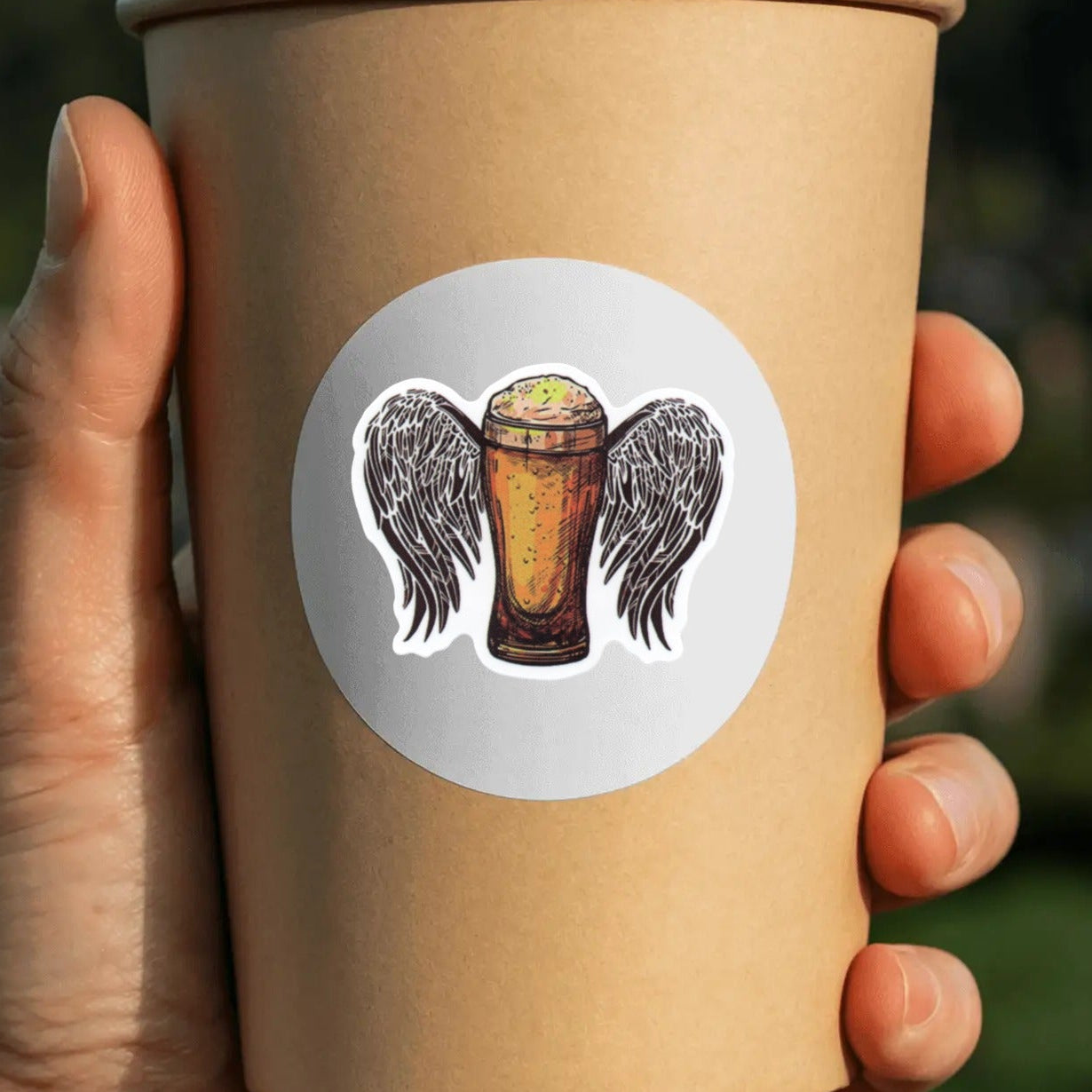 Hand holding a brown paper cup with a decorative label featuring wings and a beer.