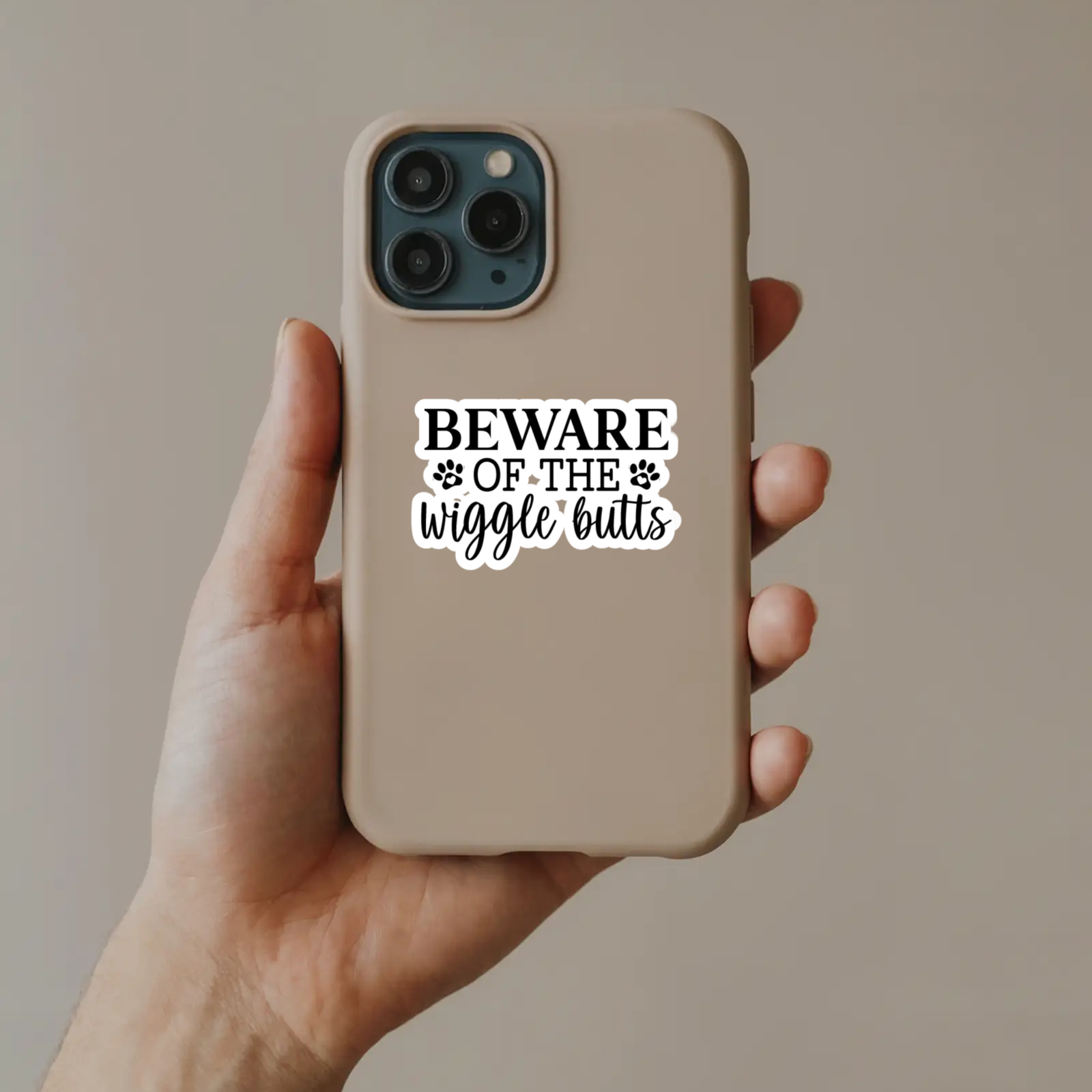 Phone case with 'Beware of the wiggle butts' text held by a hand against a plain background