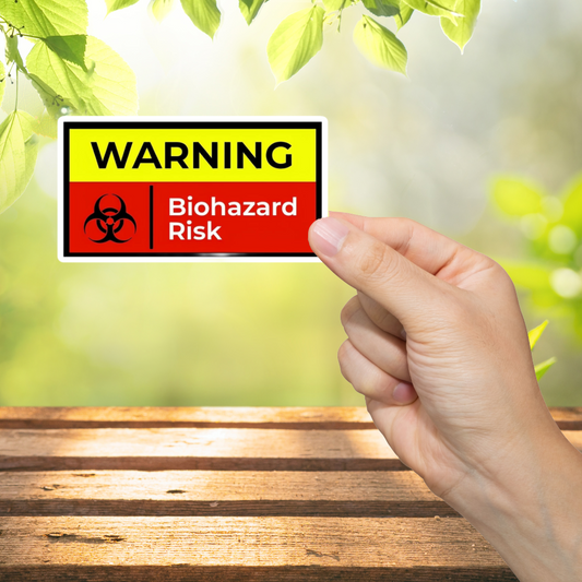 Hand holding a warning sign with biohazard symbol and text against a blurred green outdoor background