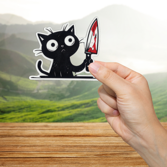 Hand holding a sticker of a black cat with a knife over a scenic background