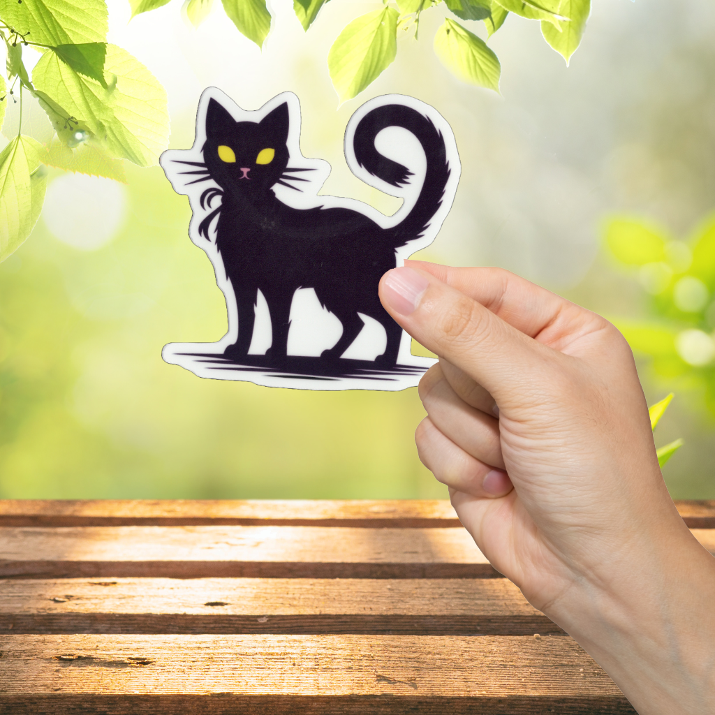 Hand holding a black cat sticker with a blurred green outdoor background