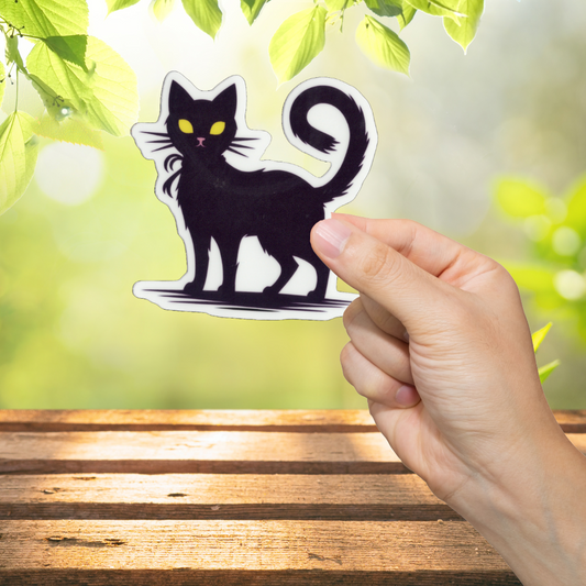 Hand holding a black cat sticker with a blurred green outdoor background