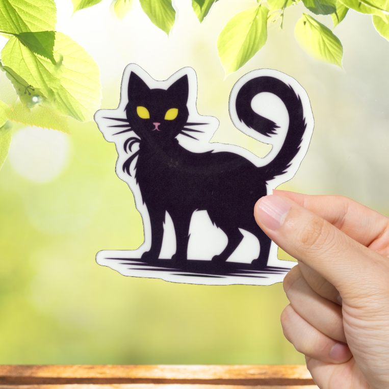 Hand holding a black cat sticker with a blurred green outdoor background