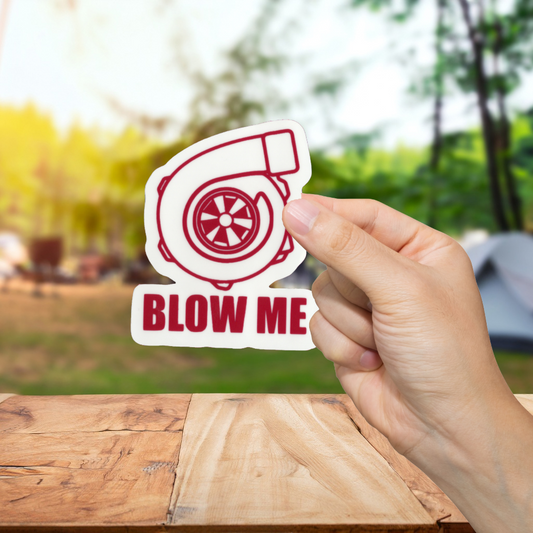 Hand holding a 'BLOW ME' turbo sticker with a blurred outdoor background
