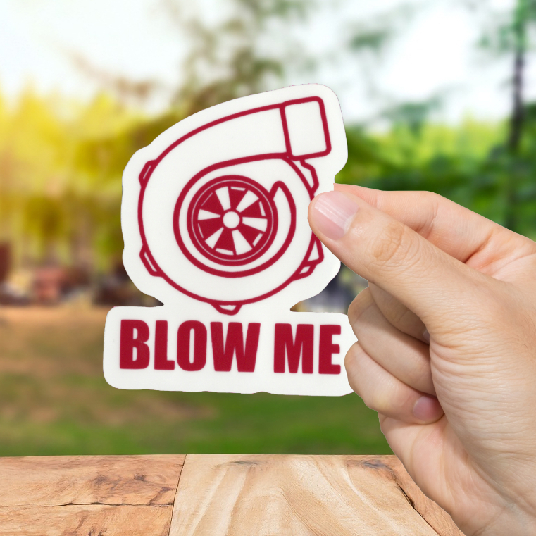 Hand holding a 'BLOW ME' turbo sticker with a blurred outdoor background