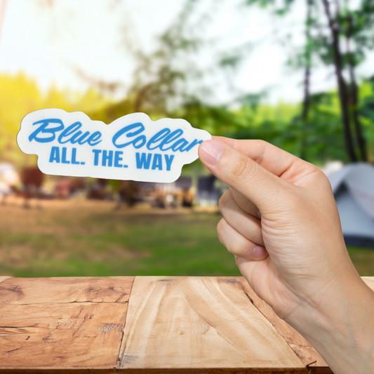 Hand holding a 'Blue Collar All. The. Way' sticker with a blurred outdoor background
