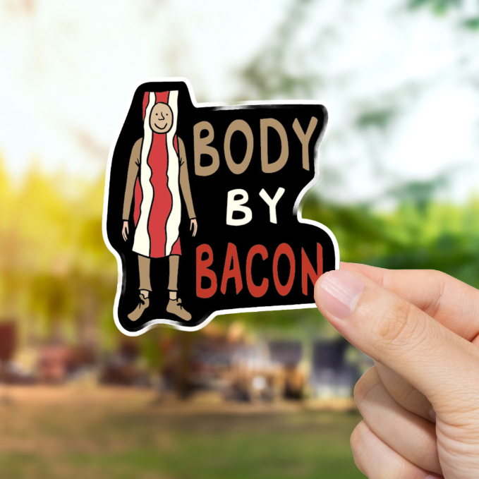 Hand holding a 'Body by Bacon' sticker with a blurred outdoor background