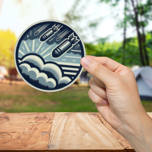 Hand holding a circular sticker with a design of missiles and waves on a wooden surface with a blurred natural background.