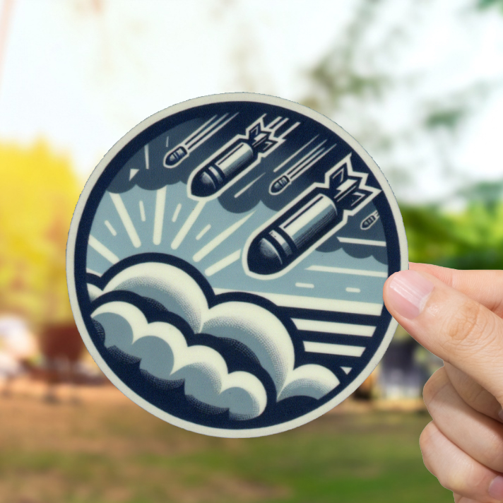 Hand holding a circular sticker with a design of missiles and waves on a wooden surface with a blurred natural background.
