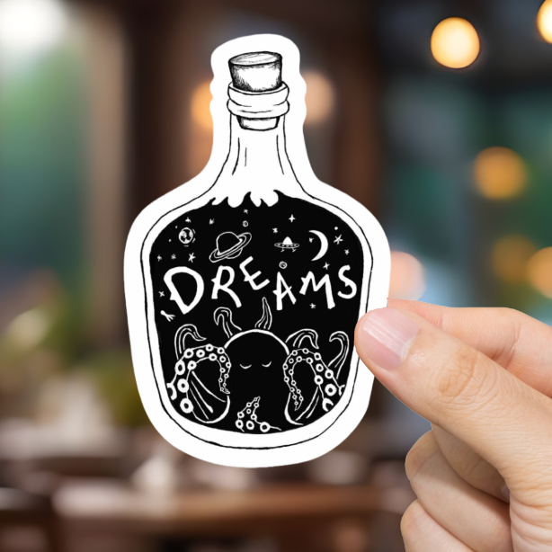 Hand holding a sticker of a bottle labeled 'Dreams' in a blurred restaurant setting