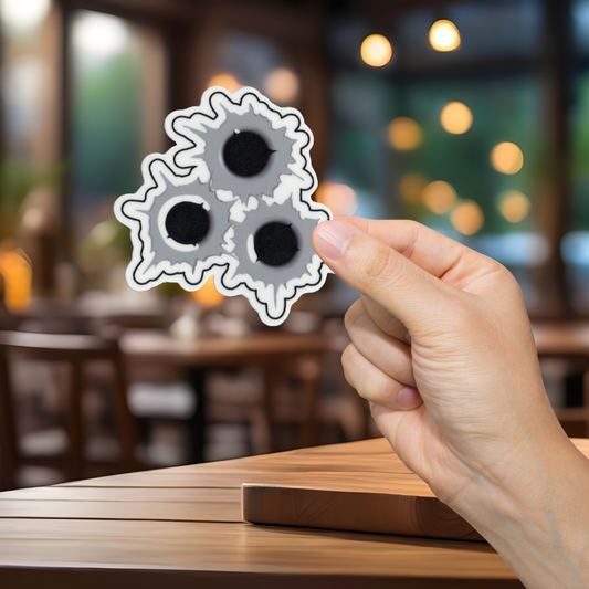 Hand holding a sticker with bullet holes in a blurred restaurant setting