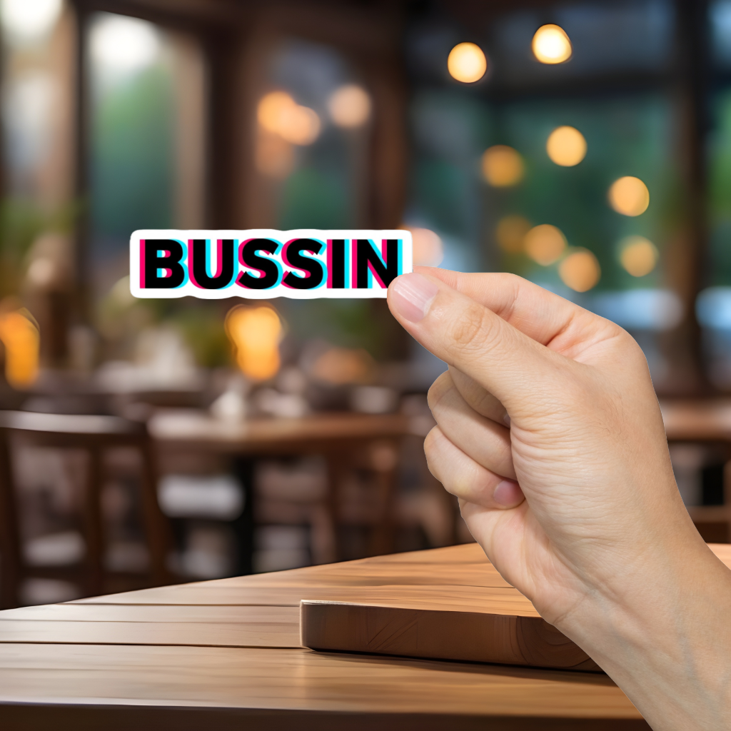 Hand holding a card with 'BUSSIN' text in a blurred restaurant setting