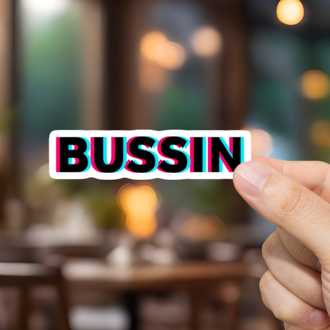 Hand holding a card with 'BUSSIN' text in a blurred restaurant setting