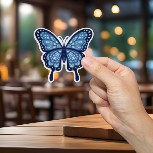 Hand holding a blue butterfly sticker with a blurred restaurant background