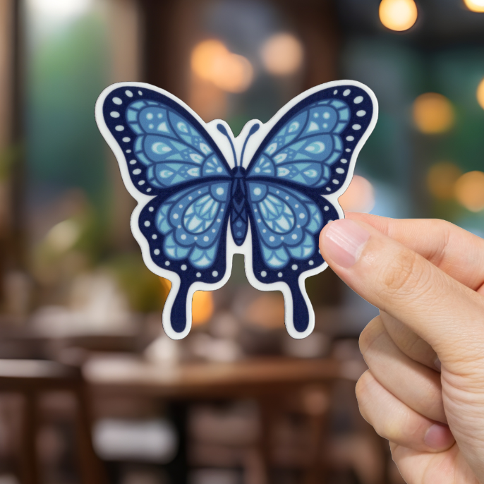 Hand holding a blue butterfly sticker with a blurred restaurant background
