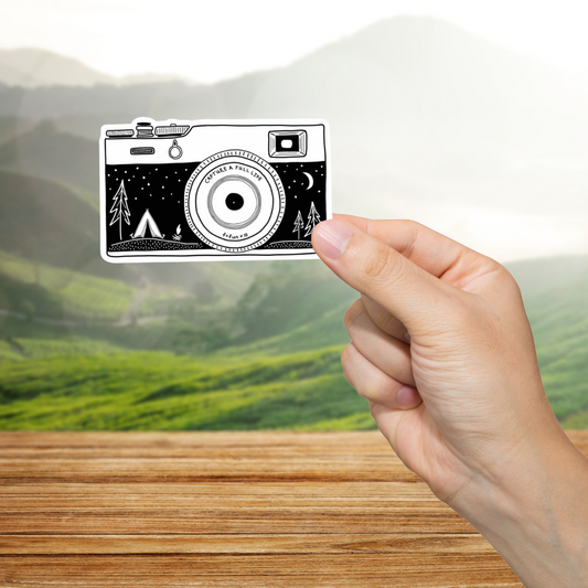 Hand holding a card with a camera design over a scenic background