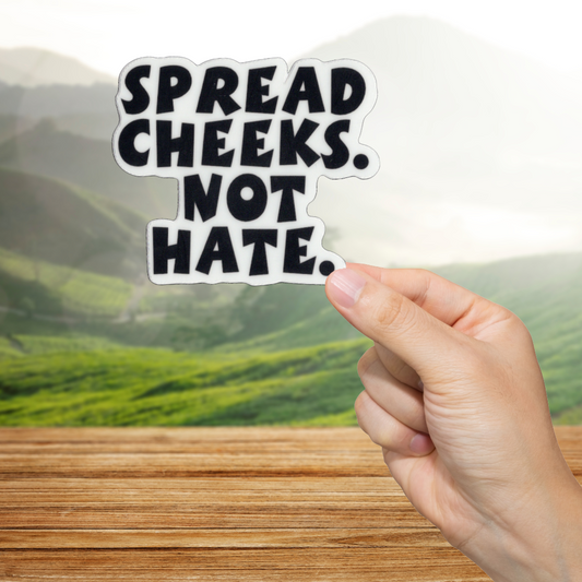 Hand holding a sticker with 'Spread Cheeks. Not Hate.' text against a scenic background