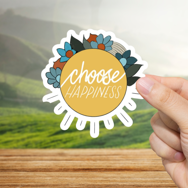 Hand holding a 'Choose Happiness' sticker with a scenic background