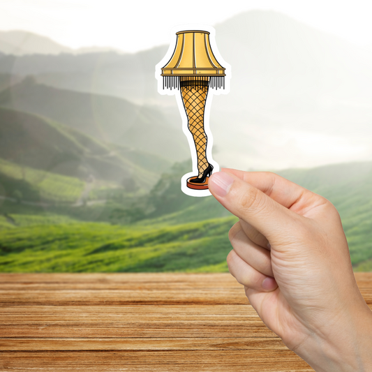 Hand holding a leg lamp sticker with a mountainous landscape in the background