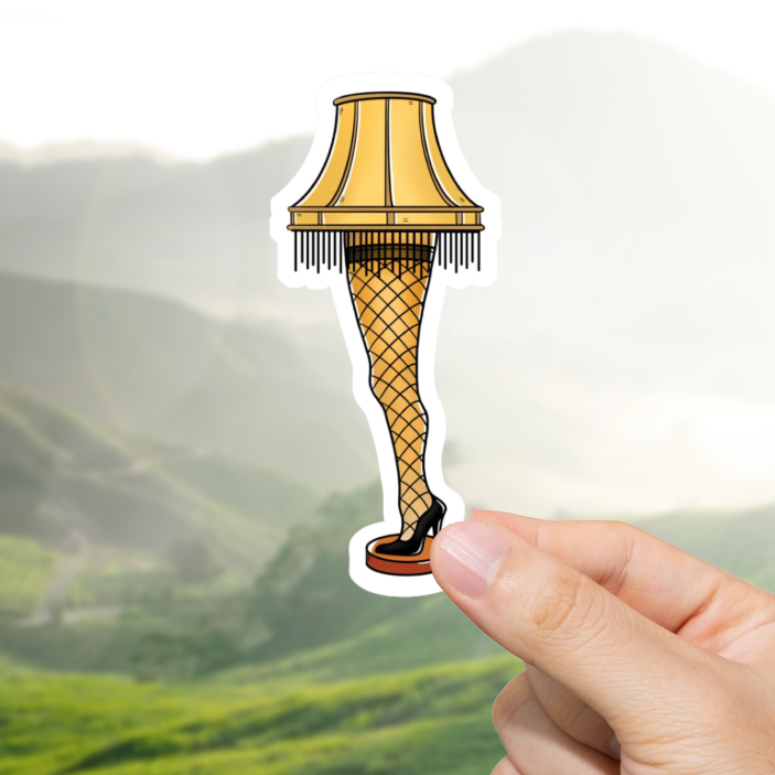 Hand holding a leg lamp sticker with a mountainous landscape in the background