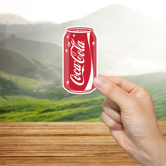 Hand holding a Coca-Cola can with a scenic background