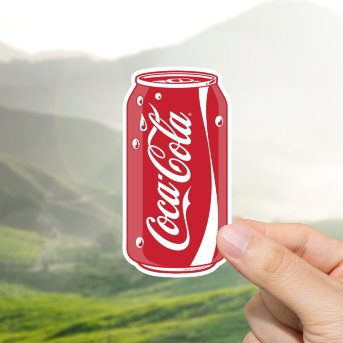 Hand holding a Coca-Cola can with a scenic background