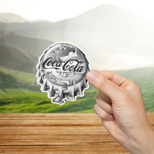 Coca-Cola bottle cap sticker held by a hand with a scenic background