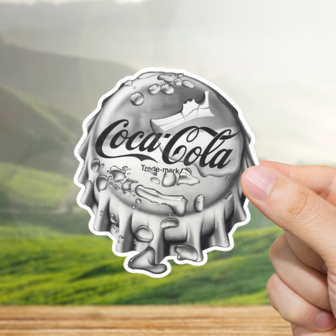 Coca-Cola bottle cap sticker held by a hand with a scenic background