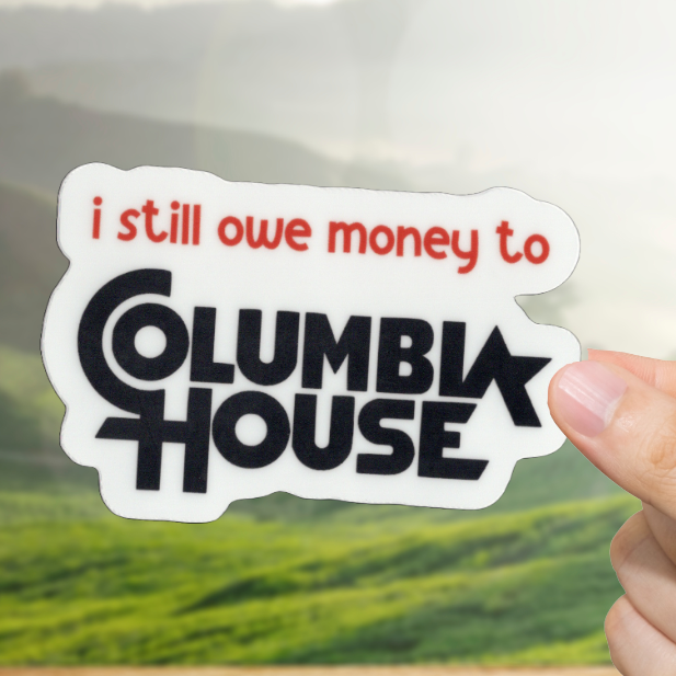 Hand holding a sticker with 'i still owe money to Columbia House' text against a scenic background