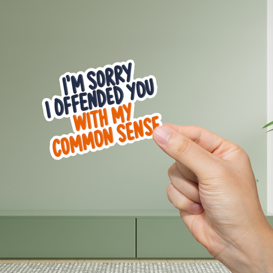 Hand holding a sticker with text 'I'm sorry I offended you with my common sense' against a green background