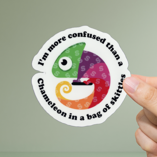 Hand holding a round sticker with a colorful chameleon design and text on a light green background