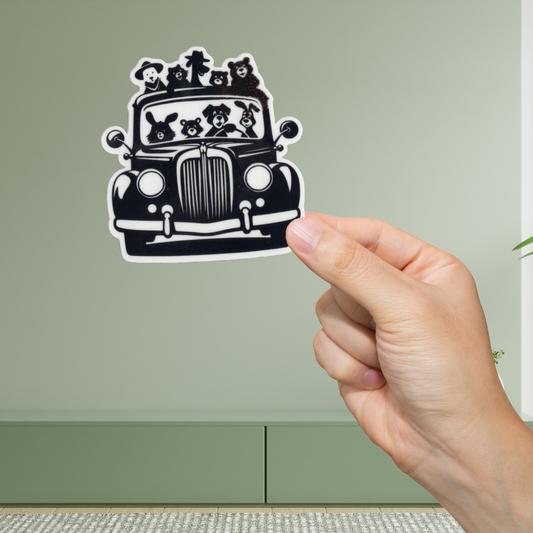Hand holding a black and white sticker of a vintage car with dog illustrations against a light green background.