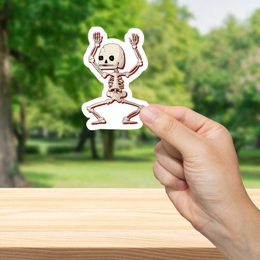 Hand holding a dancing skeleton sticker with a blurred green outdoor background