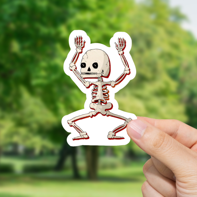 Hand holding a dancing skeleton sticker with a blurred green outdoor background