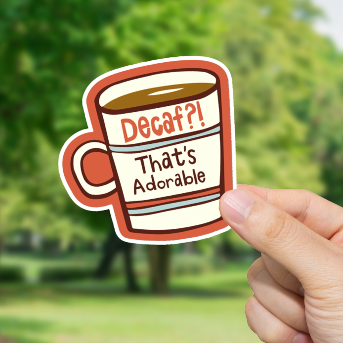 Hand holding a sticker with a coffee cup design outdoors. Decaf!? Thats Adorable."
