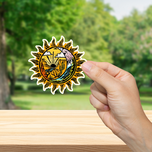 Hand holding a sun-shaped sticker with nature design against a blurred green outdoor background