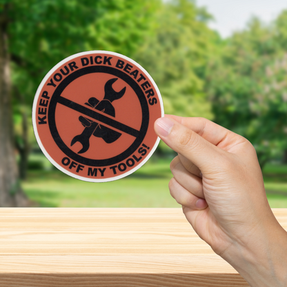 Sticker with text 'Keep your dick beaters off my tools!' held by a hand outdoors.