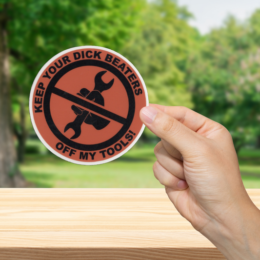 Sticker with text 'Keep your dick beaters off my tools!' held by a hand outdoors.