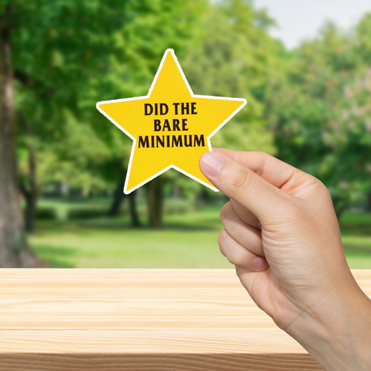 Hand holding a yellow star-shaped sign with text 'Did the bare minimum' against a blurred green outdoor background