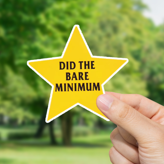 Hand holding a yellow star-shaped sign with text 'Did the bare minimum' against a blurred green outdoor background