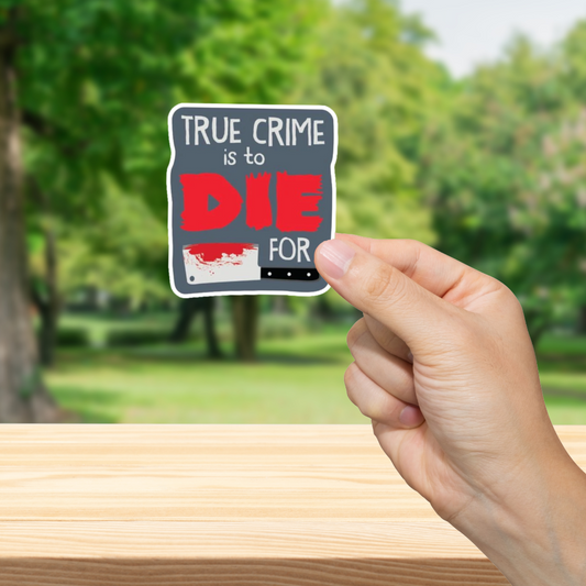 Hand holding a 'True Crime is to Die for' sticker with a blurred green outdoor background