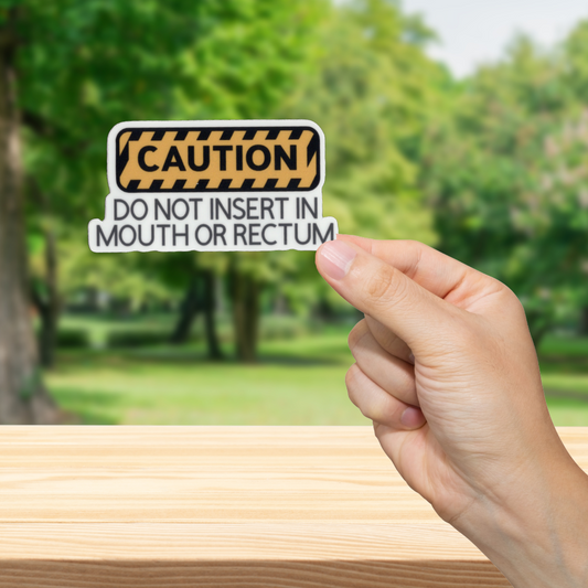 Hand holding a 'Caution' sign with 'Do not insert in mouth or rectum' and a blurred green outdoor background